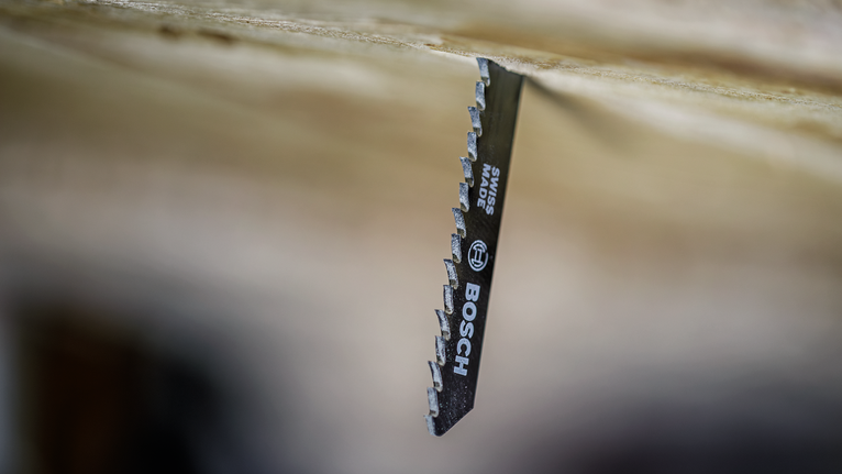 Jigsaw blade cutting through a wooden board.