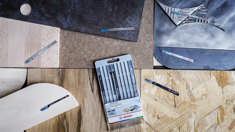 Assorted jigsaw blades displayed on different material surfaces with one multipack in the center.