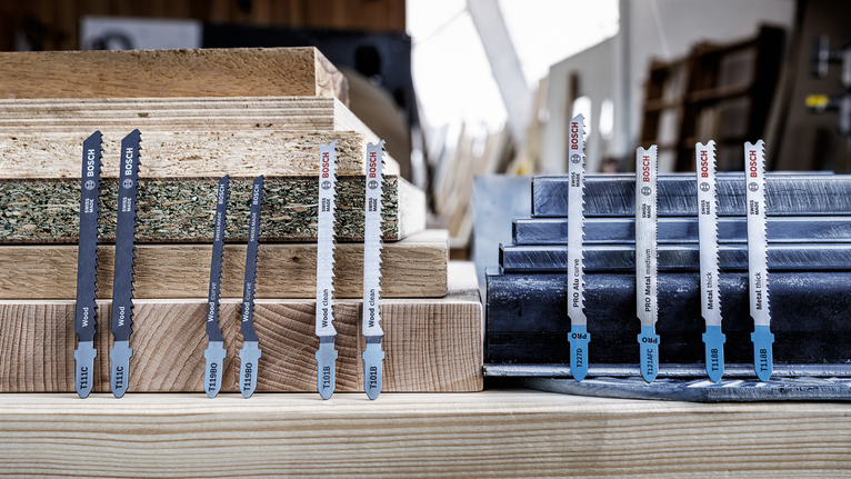 Jigsaw blades displayed upright on stacked wood and metal sheets in a workshop.