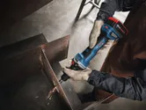 A person wearing safety equipment grinds a metal beam with a cordless straight grinder.