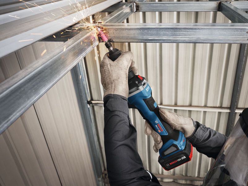 A person wearing safety equipment grinds a steel beam with a cordless straight grinder.