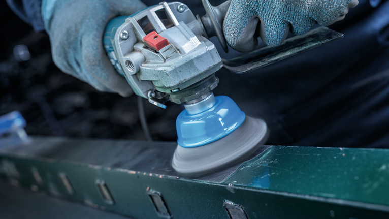 Person wearing safety equipment polishes a metal surface with a power tool.