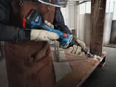 A person wearing safety equipment grinds a metal beam with a cordless straight grinder.