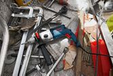 Impact drill with auxiliary handle placed on a metal workbench among scattered tools.