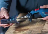 A person holds a cordless soldering iron with a protective cap on a wooden table.