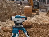 Laser leveling tool on a tripod at a construction site with an excavator in the background.