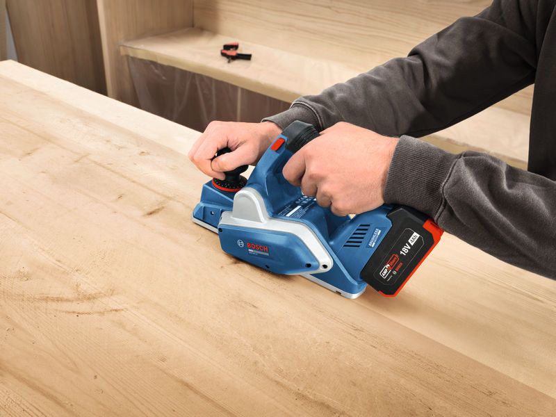 Person using a cordless planer to smooth a wooden surface.