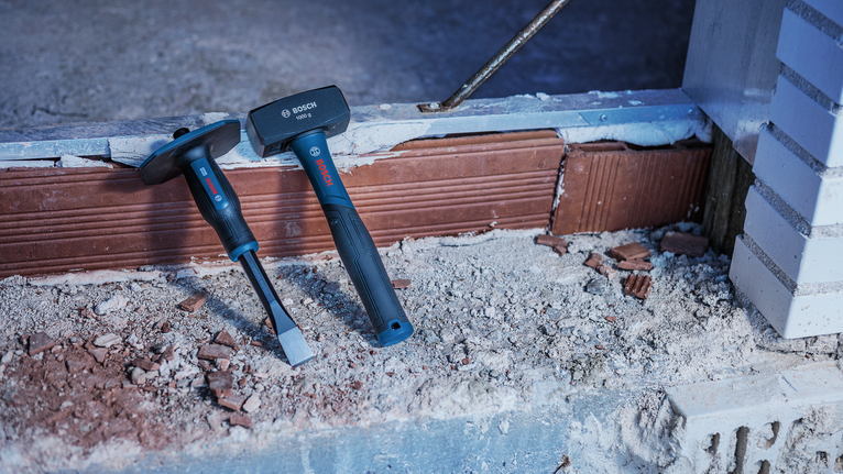 Masonry hammer and chisel resting on a dusty brick surface at a construction site.