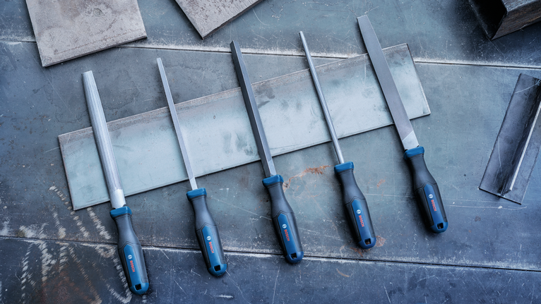 Five metal files with blue handles arranged on a metal work surface.