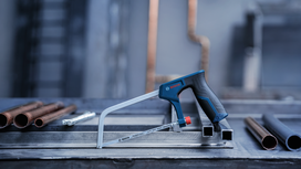 Hacksaw placed on a metal workbench near copper pipes in an industrial setting.