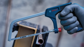 Person wearing safety equipment holds a hacksaw near a metal pipe.