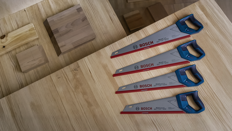 Four hand saws with blue handles are arranged on a wooden workbench.