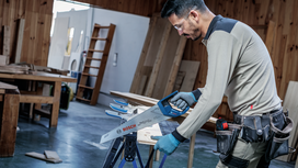 Person wearing safety equipment uses a power saw to cut wood in a workshop.