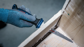 Person wearing safety equipment uses a power saw to cut a wooden panel.