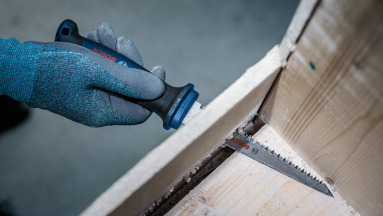 Person wearing safety equipment uses a power saw to cut a wooden panel.