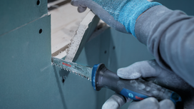 Person wearing safety equipment cuts drywall with a reciprocating saw.