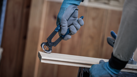 Person wearing safety equipment removes a nail from wood with pliers.