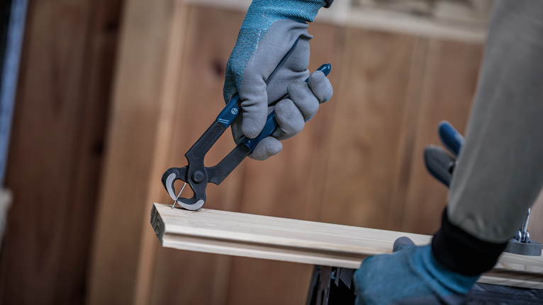 Person wearing safety equipment removes a nail from wood with pliers.