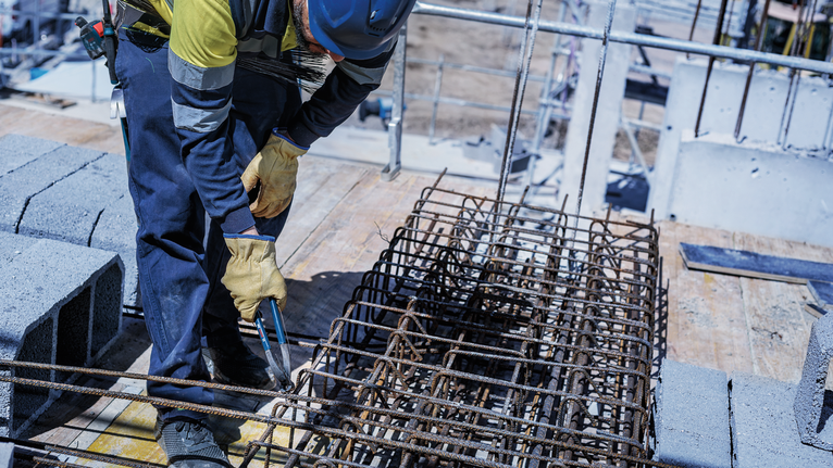Person wearing safety equipment tightens rebar on a construction site.