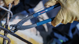 Person wearing safety equipment uses pliers to cut construction wire.