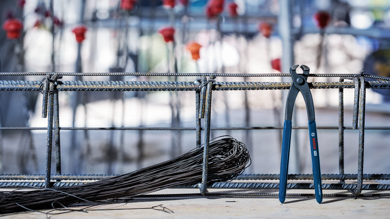 Pliers resting on rebar beside a coil of wire at a construction site.