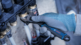Person wearing safety equipment adjusts a pipe fitting with a wrench.