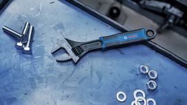Adjustable wrench lying on a work surface beside bolts, washers, and nuts.