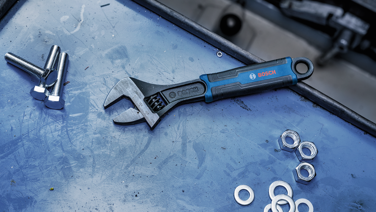Adjustable wrench lying on a work surface beside bolts, washers, and nuts.