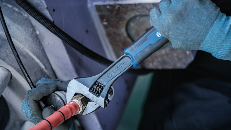 Person wearing safety equipment tightens a pipe fitting with an adjustable wrench.
