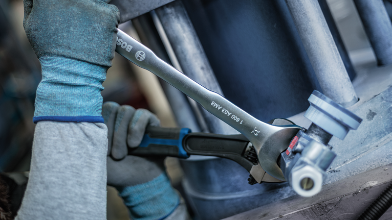 Person wearing safety equipment tightens a pipe joint with two wrenches.