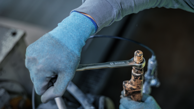 Person wearing safety equipment tightens a metal valve with a wrench.