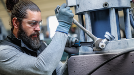 Person wearing safety equipment uses a wrench to tighten a large industrial machine.