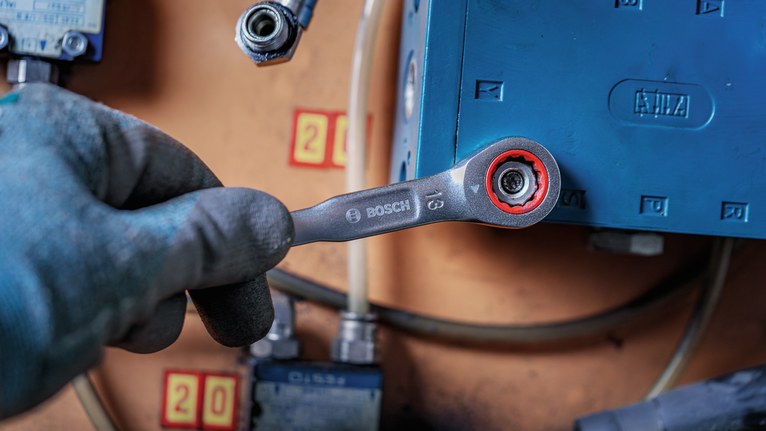 Person wearing safety equipment tightens a bolt with a ratcheting wrench.