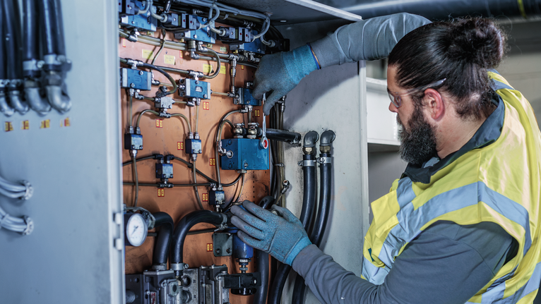 A person wearing safety equipment adjusts wiring inside an industrial control panel.