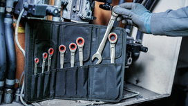 Person wearing safety equipment selects a wrench from a tool pouch.
