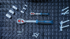 Two ratchet wrenches surrounded by sockets and bolts on a rubber mat.