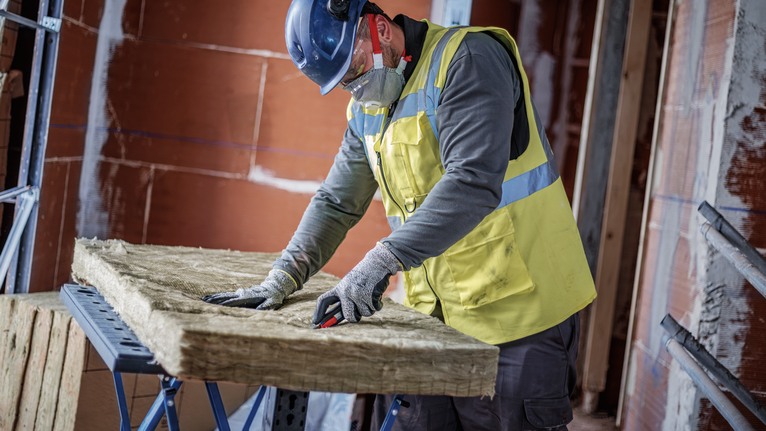 Person wearing safety equipment cuts insulation material on a workbench.
