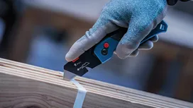 Person wearing safety equipment uses a utility knife to cut strapping on wood.