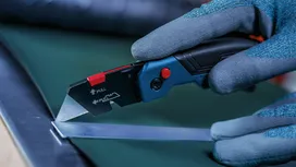 Person wearing safety equipment uses a utility knife to cut sheet material.