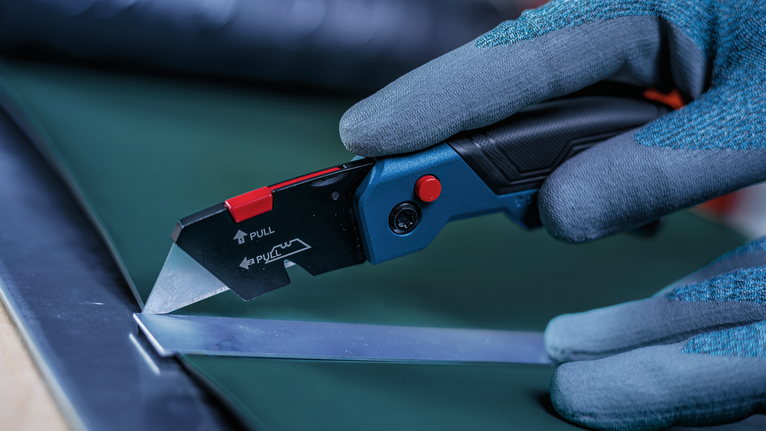 Person wearing safety equipment uses a utility knife to cut sheet material.