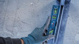 Person wearing safety equipment checks level alignment on a metal rail.