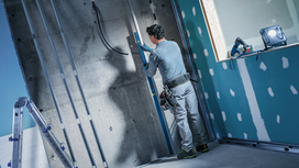 Person wearing safety equipment uses a spirit level to check alignment on a concrete wall.