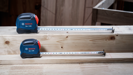Two tape measures extended on stacked wooden beams in a workshop.