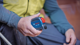 Person wearing safety equipment holds a tape measure during construction work.