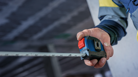 Person wearing safety equipment extends a tape measure at a construction site.
