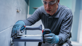 Person wearing safety equipment measures and marks a wall pipe with a tape measure.