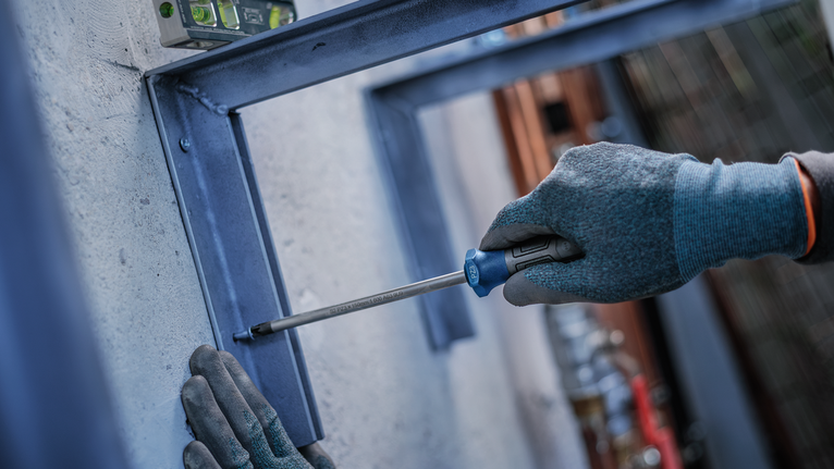 Person wearing safety equipment uses a screwdriver to fasten a metal frame.
