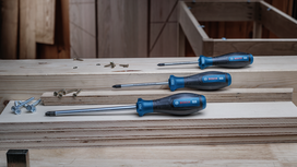 Three blue-handled screwdrivers lie on stacked wood planks beside several screws.