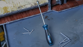 Long screwdriver placed on a metal surface with scattered screws.