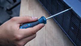 Person using a blue-handled screwdriver to tighten a screw on a metal vent.